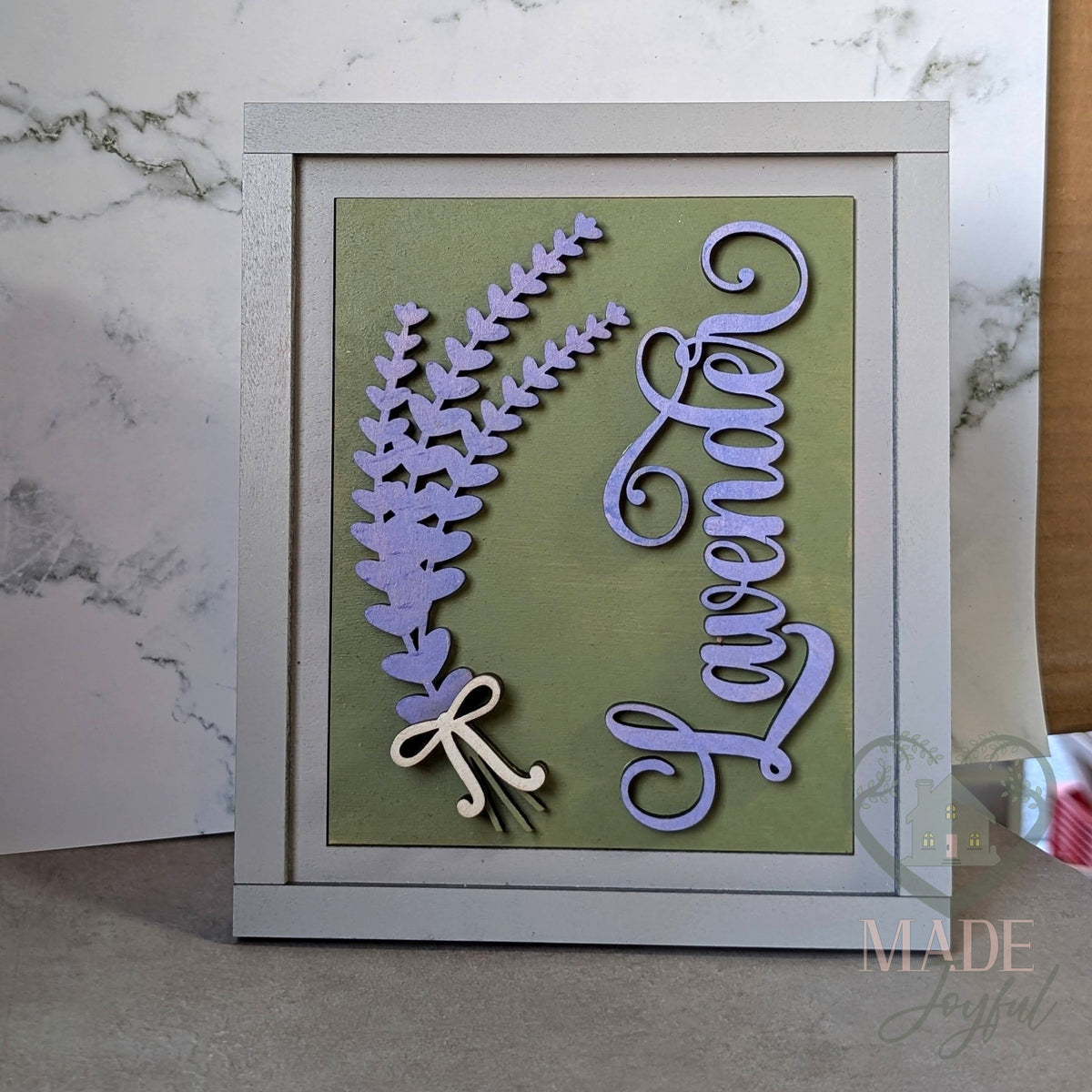 Lavender script 3D wood insert with a purple lavender sprig tied with a cream bow on a sage green background, in a gray interchangeable farmhouse frame.