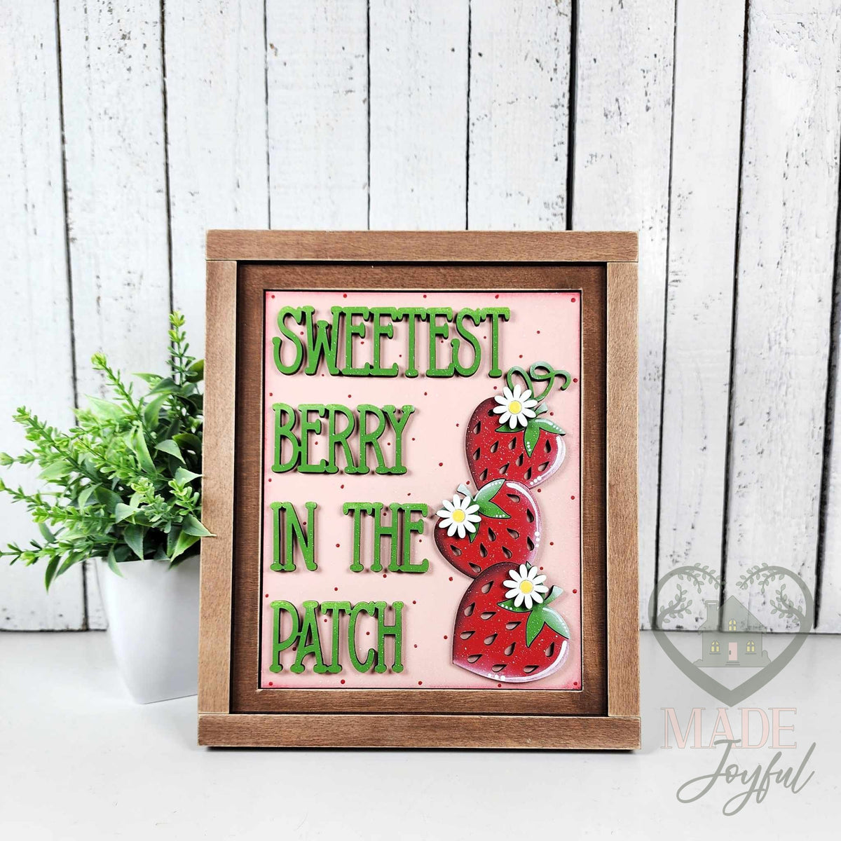 Sweetest Berry in the Patch 3D wood insert in green lettering with three stacked strawberries and daisies on a pink polka-dot background, in a stained farmhouse frame.