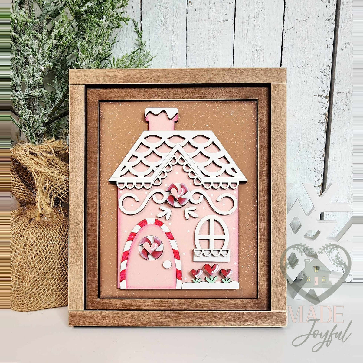 Pink gingerbread house 3D wood insert with white scalloped icing roof, candy cane door trim, and peppermint details in a stained farmhouse frame.