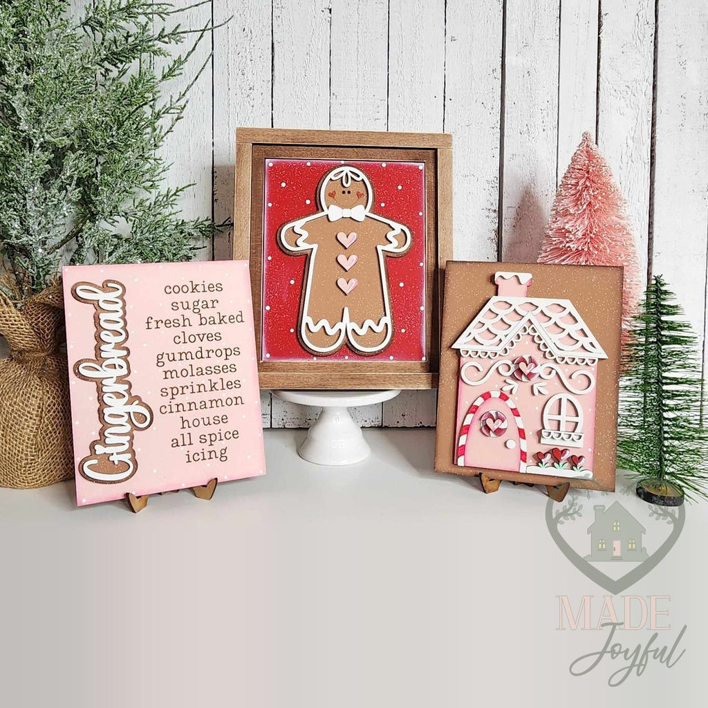 Pink Gingerbread insert trio for interchangeable farmhouse frames: a gingerbread man in a stained wood frame with a pink Gingerbread word-list sign and a candy-trimmed gingerbread house on small stands, hand-painted in Brentwood, TN.