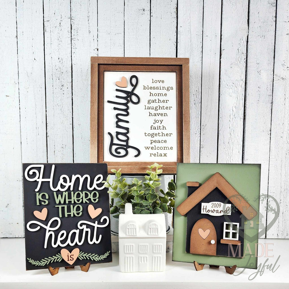 Home Is Where the Heart Is insert trio for interchangeable farmhouse frames: a Family word-list sign in a stained wood frame with a black home-heart script sign and a black house with a family name plaque on stands.