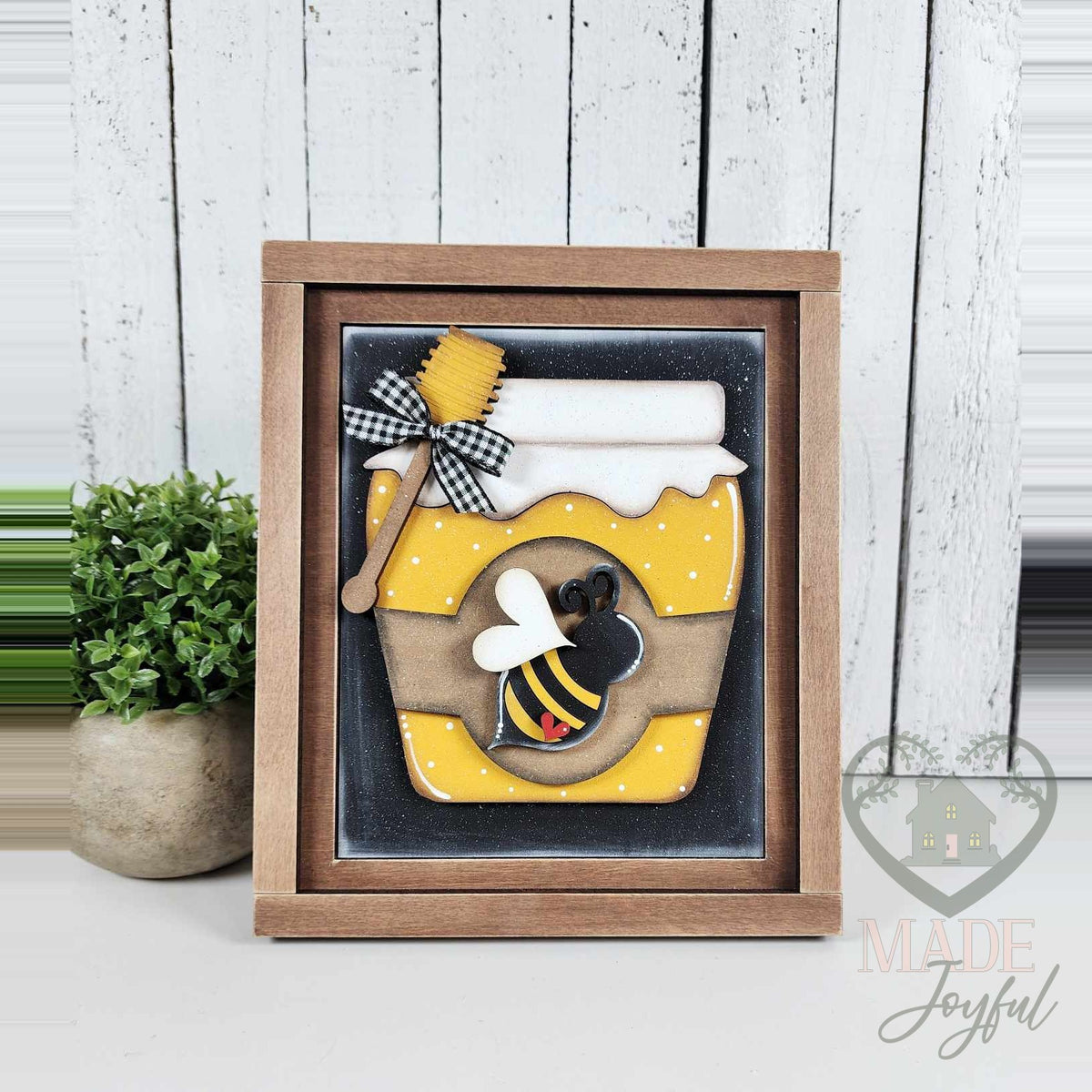 Yellow honey jar 3D wood insert with a buffalo-check bow, honey dipper, and small bee on a black polka-dot background in a stained farmhouse frame.