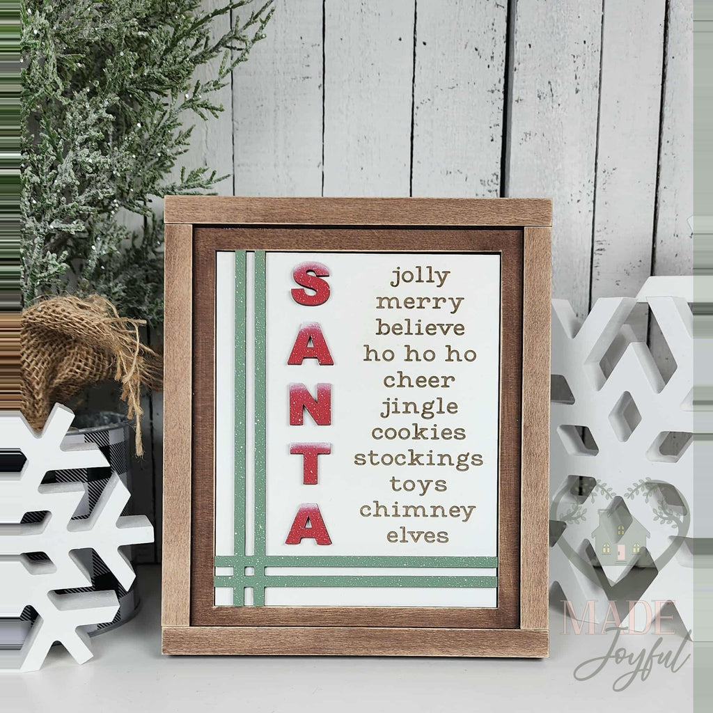 SANTA word-list insert with jolly, merry, believe, ho ho ho, cheer, jingle, cookies, stockings, toys, chimney, and elves with red letters and green stripes in a stained farmhouse frame.