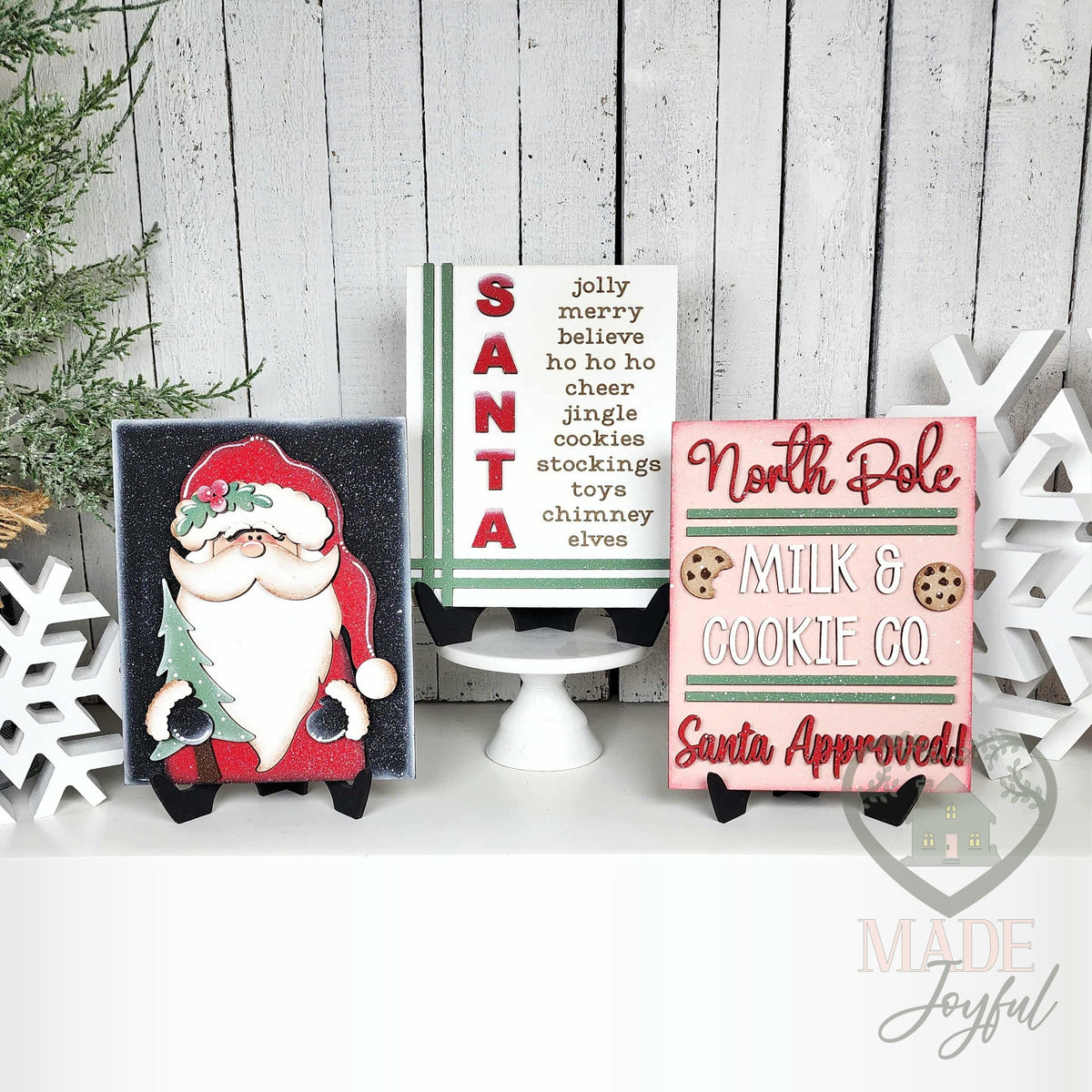 North Pole Santa insert trio for interchangeable farmhouse frames: a SANTA word-list sign on a cake stand with a woodland Santa and a North Pole Milk & Cookie Co. sign on stands, hand-painted in Brentwood, TN.