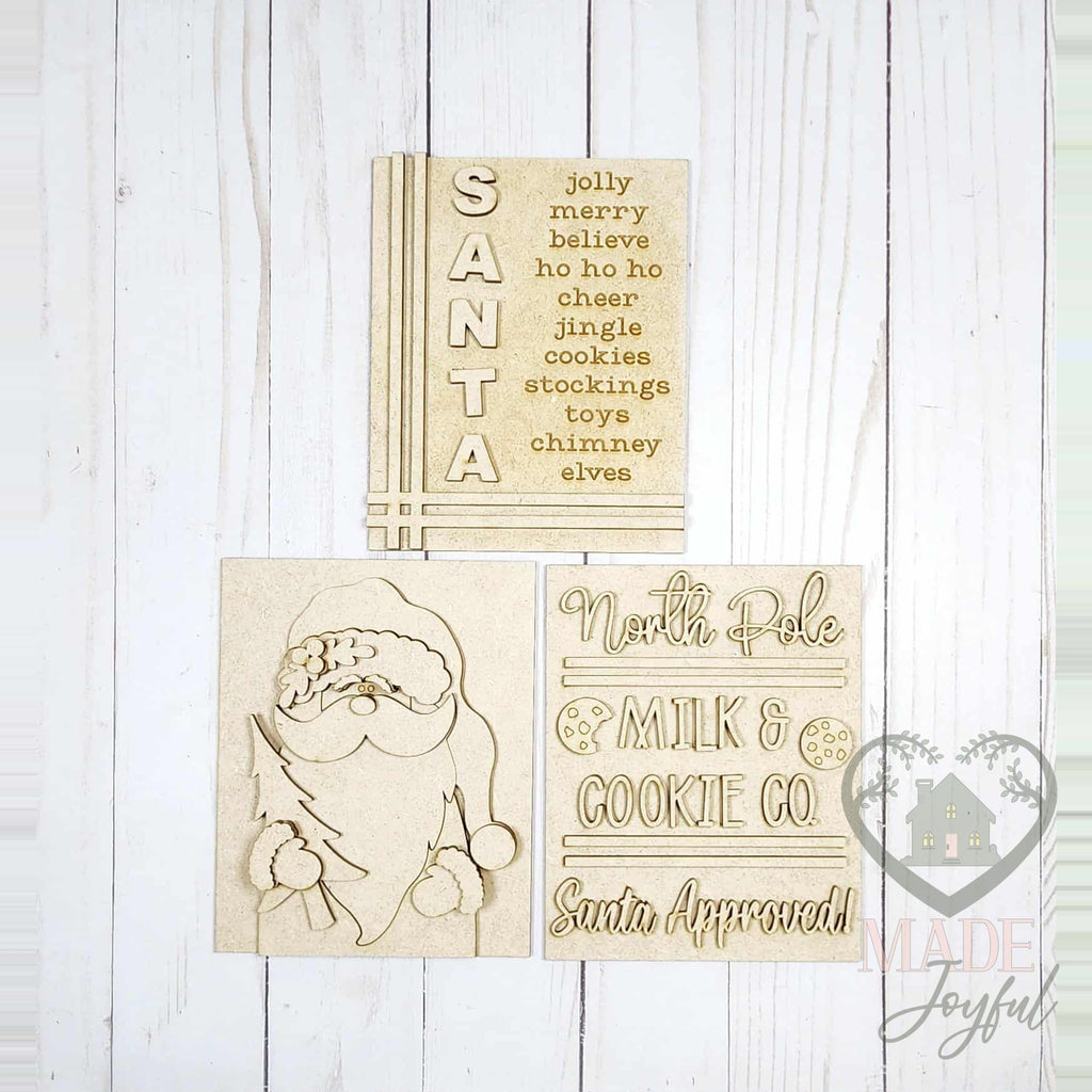 Unfinished laser-cut wood North Pole Santa trio DIY kit with SANTA word list, woodland Santa, and Milk & Cookie Co. inserts, ready to paint at a DIY party in Williamson County, TN.