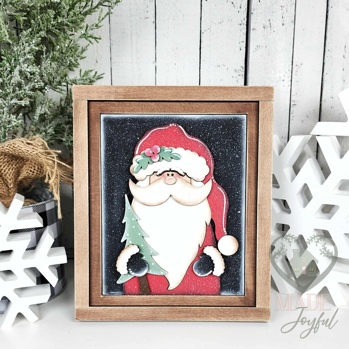 Woodland Santa 3D wood insert with a red hat, holly, white beard, and small evergreen tree on a black glitter background in a stained farmhouse frame.