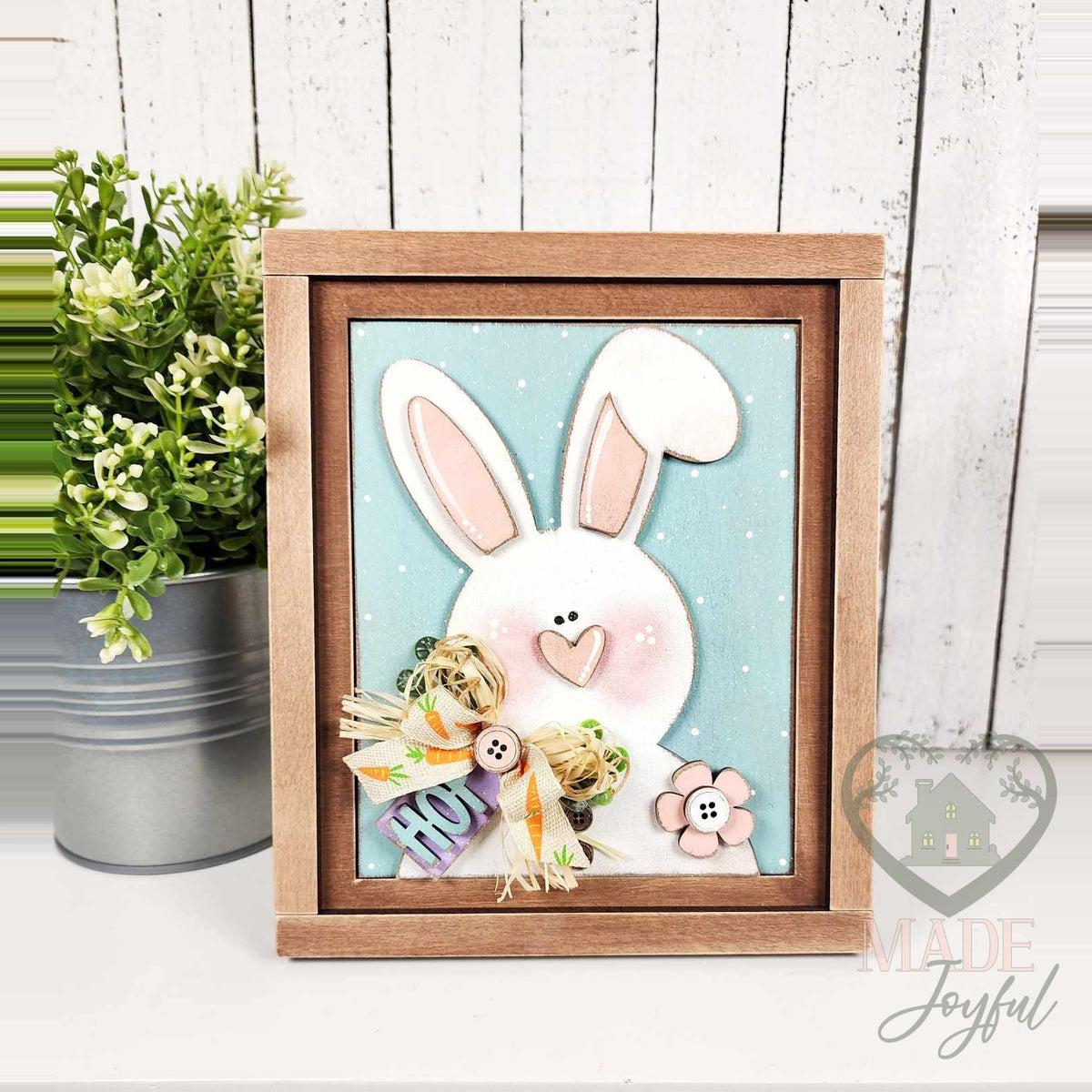 White bunny 3D wood insert with pink ears, a blush heart nose, raffia bow, and HOP tag on a blue polka-dot background in a stained farmhouse frame.