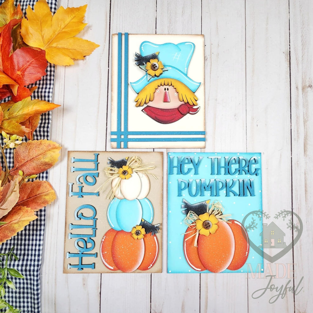 Fall Scarecrow insert trio of hand-painted 3D wood signs: a scarecrow in a teal hat, Hello Fall stacked pumpkins, and Hey There Pumpkin, styled with autumn leaves, made in Brentwood, TN.