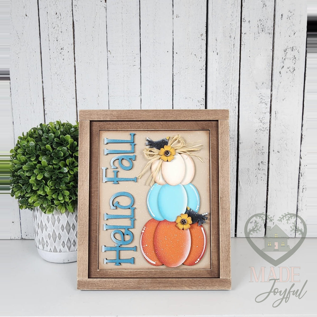 Hello Fall 3D wood insert with teal lettering and stacked white, teal, and orange pumpkins with a sunflower and crow, in a stained farmhouse frame.