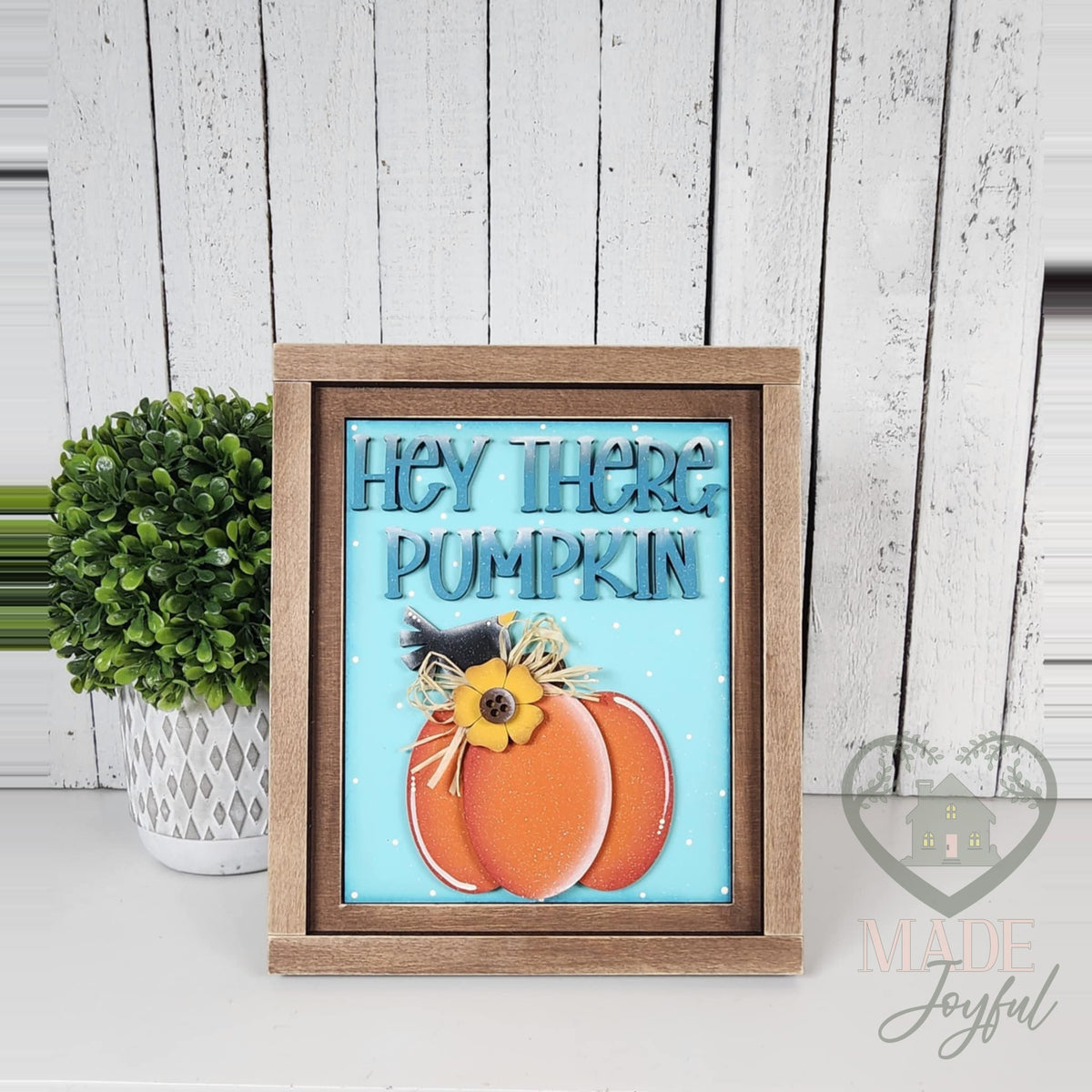 Hey There Pumpkin 3D wood insert with teal lettering and an orange pumpkin with a sunflower on a teal polka-dot background, in a stained farmhouse frame.