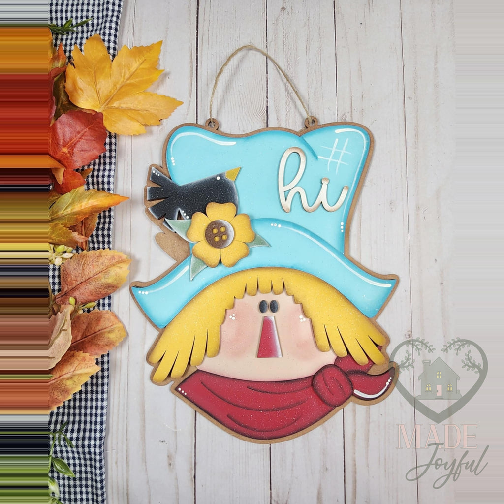 Hi Scarecrow 3D wood door hanger with a teal hat, sunflower, crow, yellow straw hair, and red scarf, styled with autumn leaves, hand-painted in Brentwood, TN.