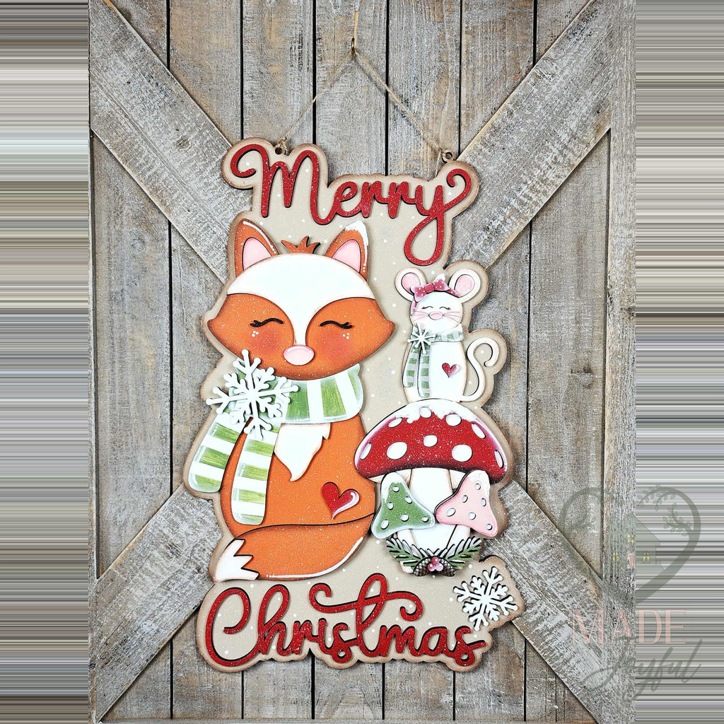 Forest Friends Merry Christmas 3D wood door hanger with a fox in a green scarf, a mouse, red toadstool mushrooms, and red script, hand-painted in Brentwood, TN.