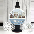 Welcome Winter Village round wood door hanger with snowy cottages, wreaths, and blue Welcome Winter script, displayed on a black stand with snowflakes, hand-painted in Brentwood, TN.
