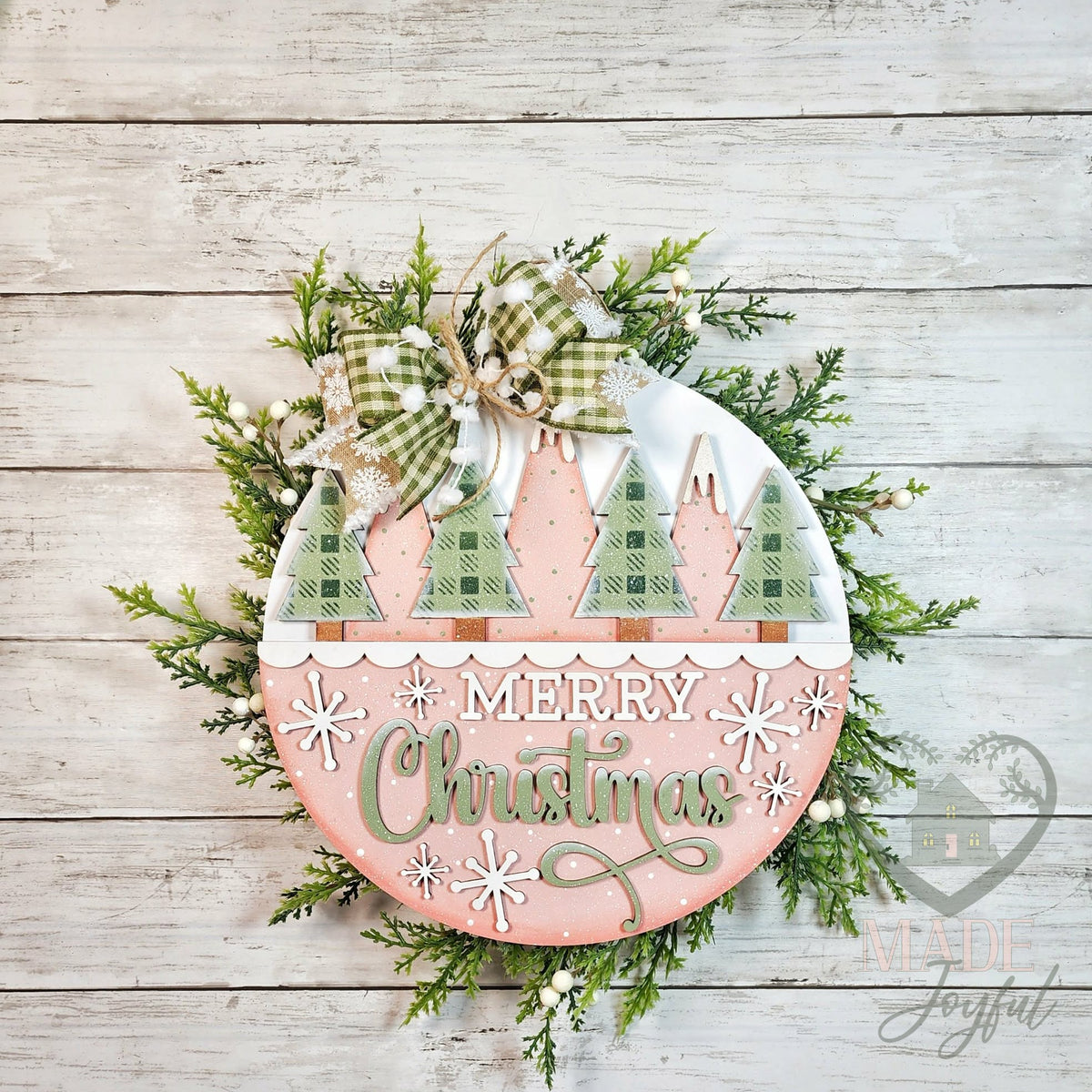 Merry Christmas Trees round wood door hanger with snowy green plaid trees and sage script on blush pink, with a green gingham bow and greenery, hand-painted in Brentwood, TN.