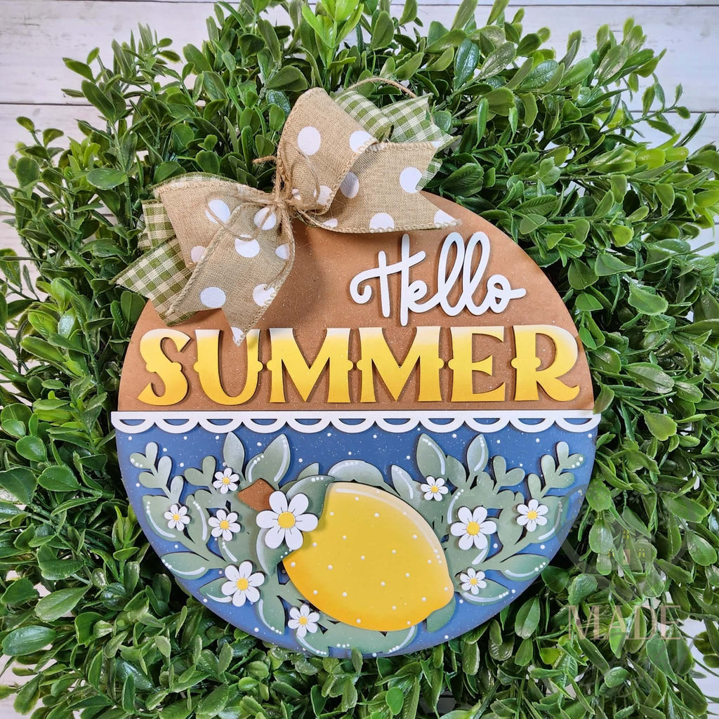 Hello Summer round wood door hanger with yellow lettering, a 3D lemon, green leaves, and white blossoms on blue, framed by greenery, hand-painted in Brentwood, TN.