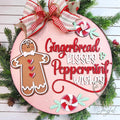 Gingerbread Kisses and Peppermint Wishes round wood door hanger with a gingerbread man, peppermints, and red script on pink, topped with a candy-stripe bow, hand-painted in Brentwood, TN.