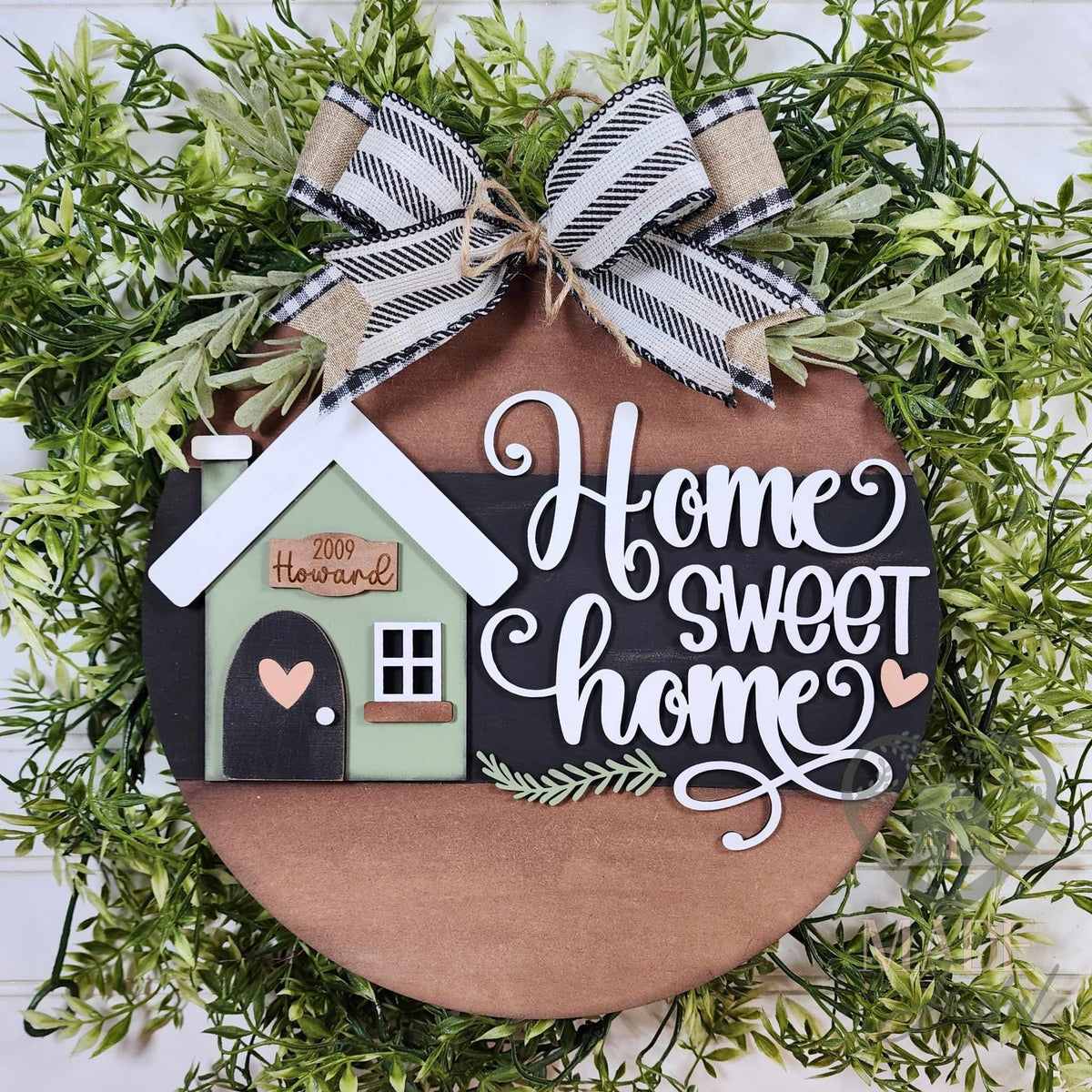 Home Sweet Home round wood door hanger with a sage house, family name plaque, and white script on black and walnut, framed by greenery, hand-painted in Brentwood, TN.