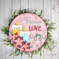 Peace Love Joy round wood door hanger with 3D candles, pink poinsettias, and snowflakes on pink, framed by greenery, hand-painted in Brentwood, TN.