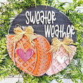 Sweater Weather round wood door hanger with knit-pattern orange and blush pumpkins, hearts, and raffia bows under white lettering on black, hand-painted in Brentwood, TN.