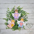 Three hand-painted 3D wood angel ornaments in purple, pink and blue with gold halos and white wings, arranged on a green wreath, hand-painted in Brentwood, TN.