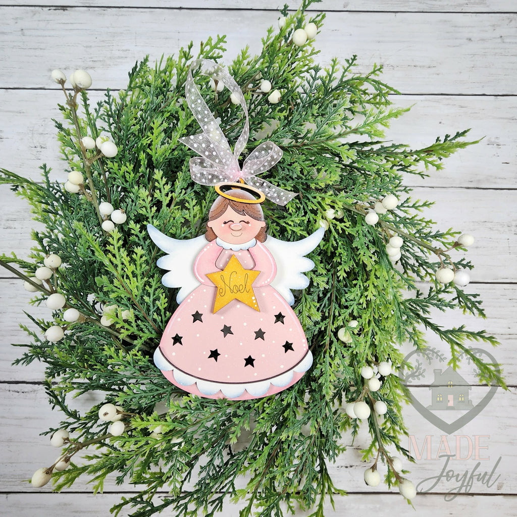 Pink angel ornament with a gold star, white wings and star cut-outs in her gown, hung with sheer ribbon on greenery, hand-painted in Brentwood, TN.