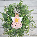 Pink angel ornament with a gold star, white wings and star cut-outs in her gown, hung with sheer ribbon on greenery, hand-painted in Brentwood, TN.