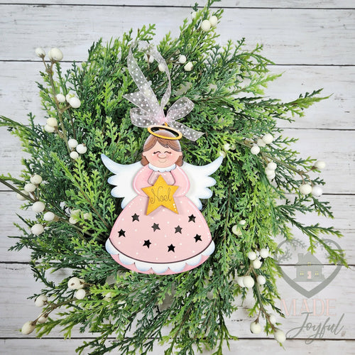 Pink angel ornament with a gold star, white wings and star cut-outs in her gown, hung with sheer ribbon on greenery, hand-painted in Brentwood, TN.
