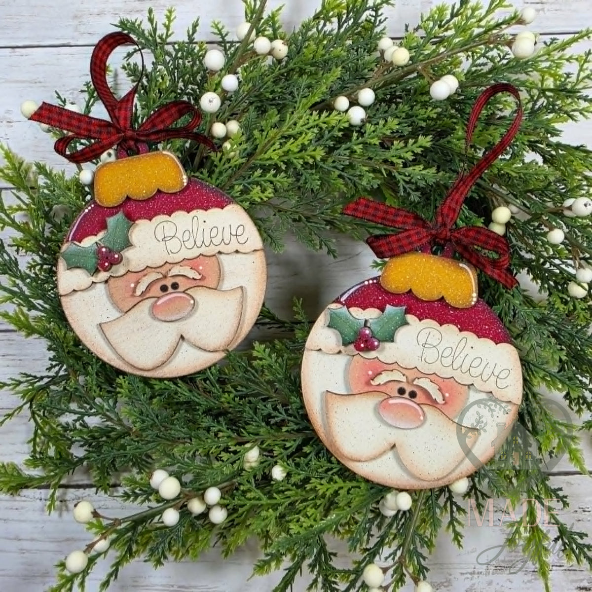 Two round Santa bulb ornaments with Believe hat bands, holly and fluffy beards, hung with plaid bows, hand-painted in Brentwood, TN.
