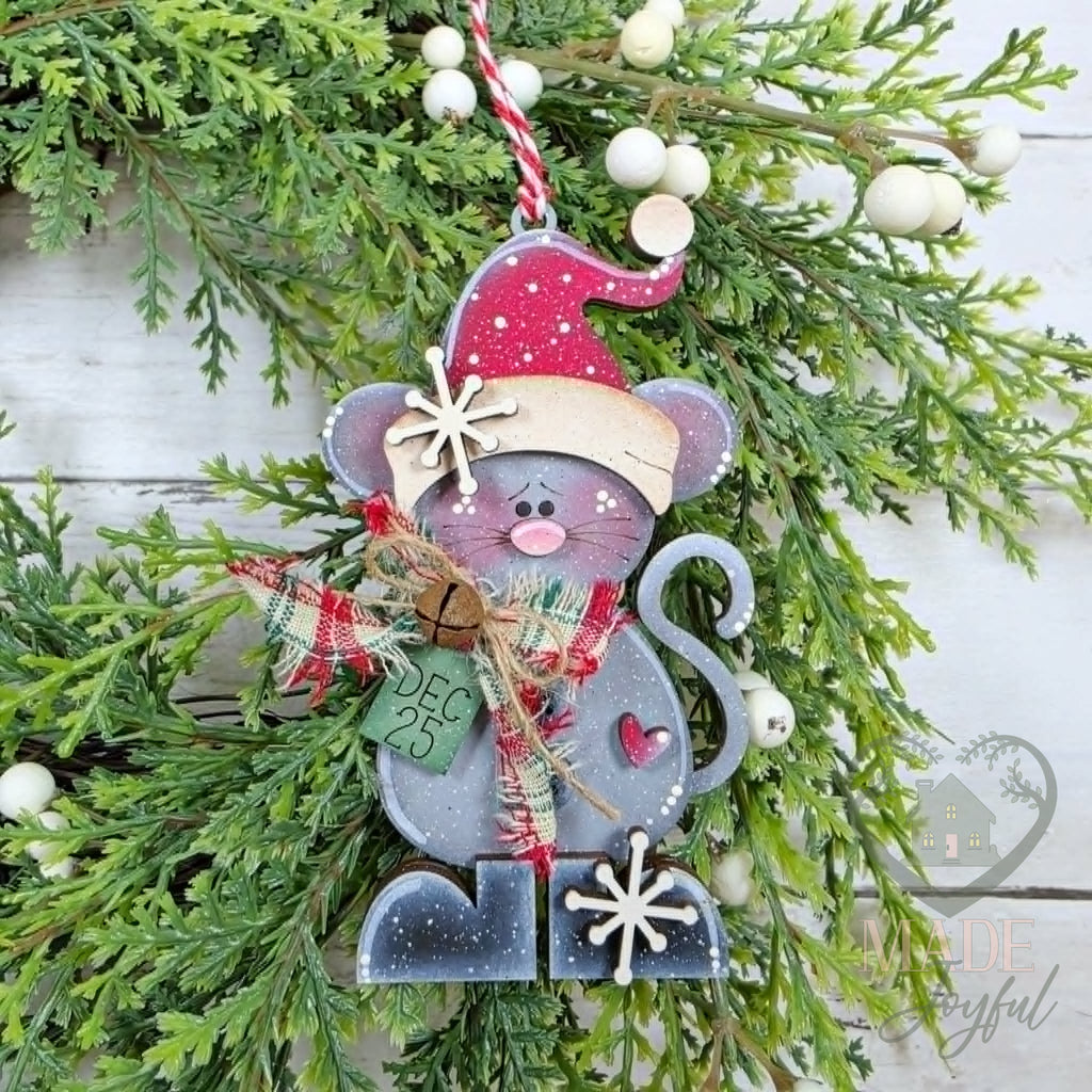 Pip the Christmas mouse ornament in a pink Santa hat with a plaid scarf and jingle bell, hung on greenery, hand-painted in Brentwood, TN.