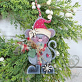 Pip the Christmas mouse ornament in a pink Santa hat with a plaid scarf and jingle bell, hung on greenery, hand-painted in Brentwood, TN.