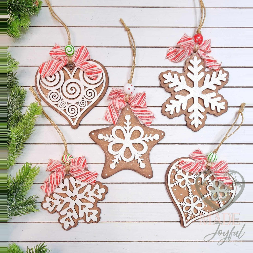 Five gingerbread cookie ornaments shaped like hearts, a star and snowflakes with white icing details and striped bows, hand-painted in Brentwood, TN.