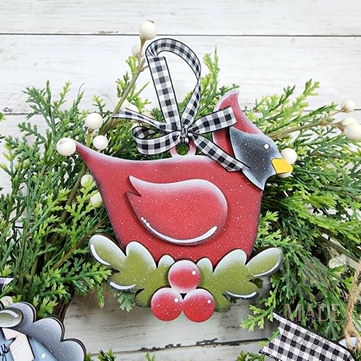Red cardinal ornament perched on holly and berries with a black and white gingham bow, hand-painted in Brentwood, TN.