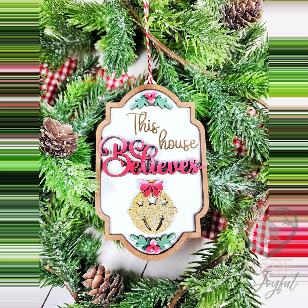 This House Believes ornament with pink script and a gold sleigh bell, hand-painted in Brentwood, TN.