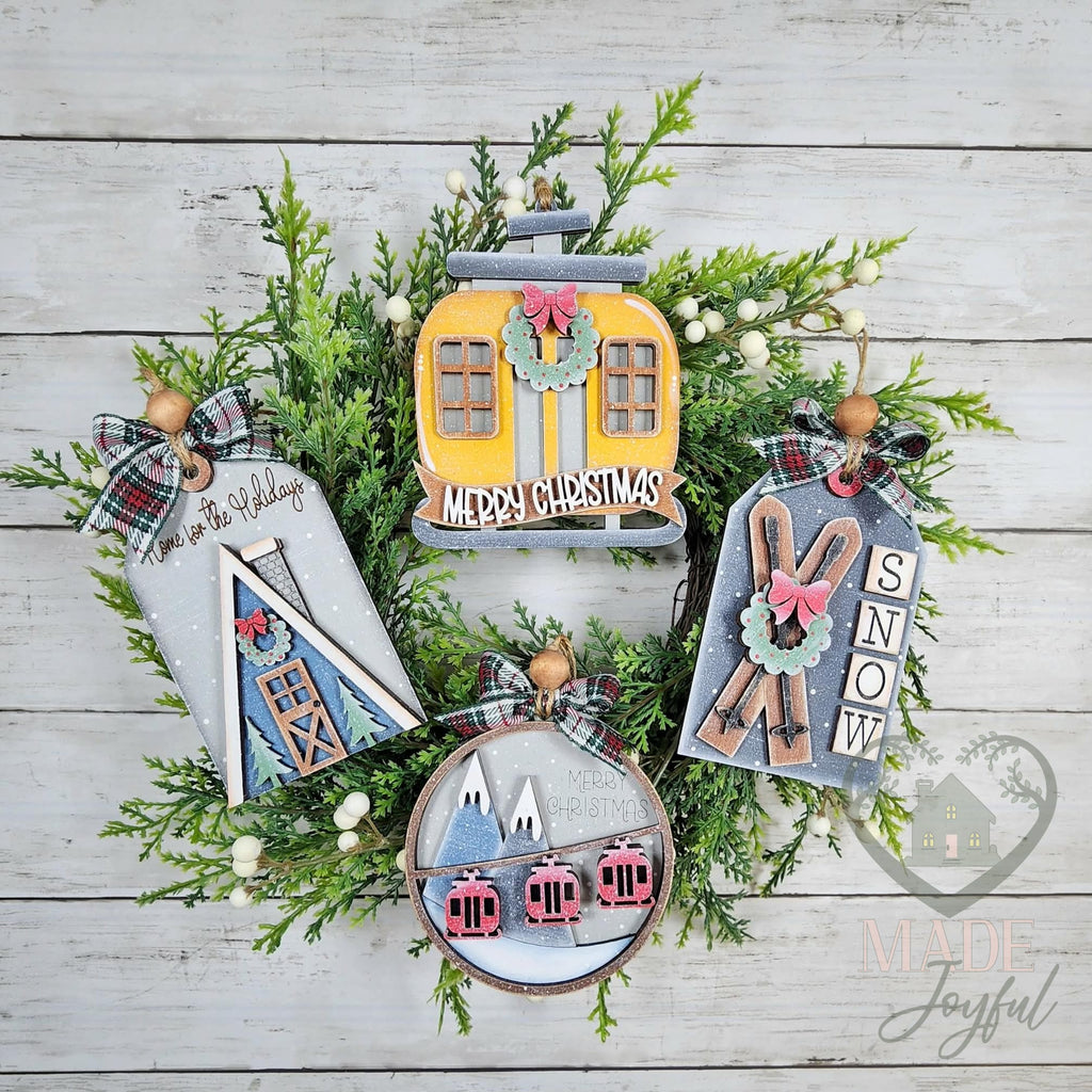 Ski lodge ornament set with an A-frame cabin tag, yellow gondola, skis SNOW tag and round ski-lift ornament on a wreath, hand-painted in Brentwood, TN.