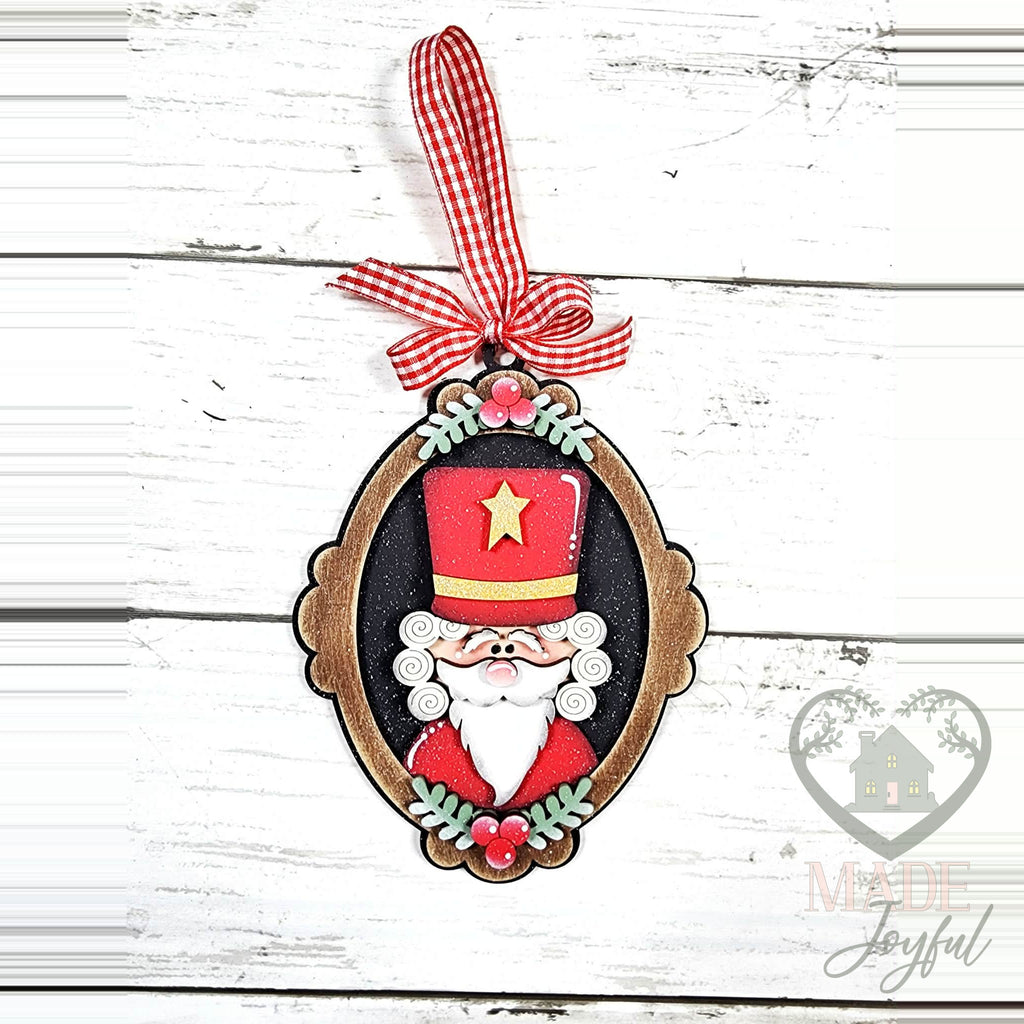 Nutcracker cameo ornament in an oval frame with holly and a red gingham bow, hand-painted in Brentwood, TN.