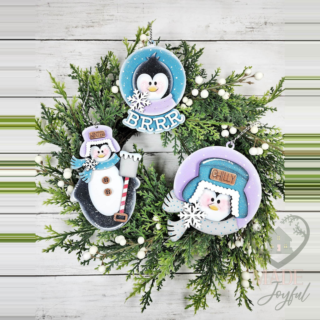 Three penguin ornaments with a BRRR round, a Chilly penguin in a trapper hat and a standing penguin, on a wreath, hand-painted in Brentwood, TN.