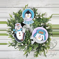 Three penguin ornaments with a BRRR round, a Chilly penguin in a trapper hat and a standing penguin, on a wreath, hand-painted in Brentwood, TN.