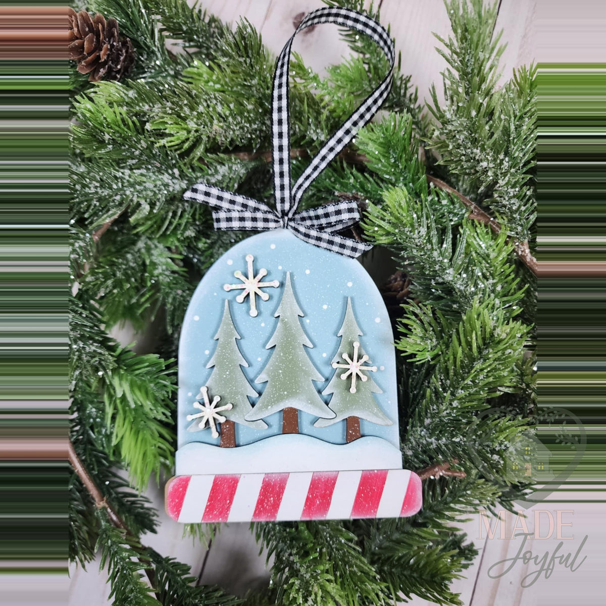 Snow globe ornament with pine trees and a candy-stripe base, hand-painted in Brentwood, TN.