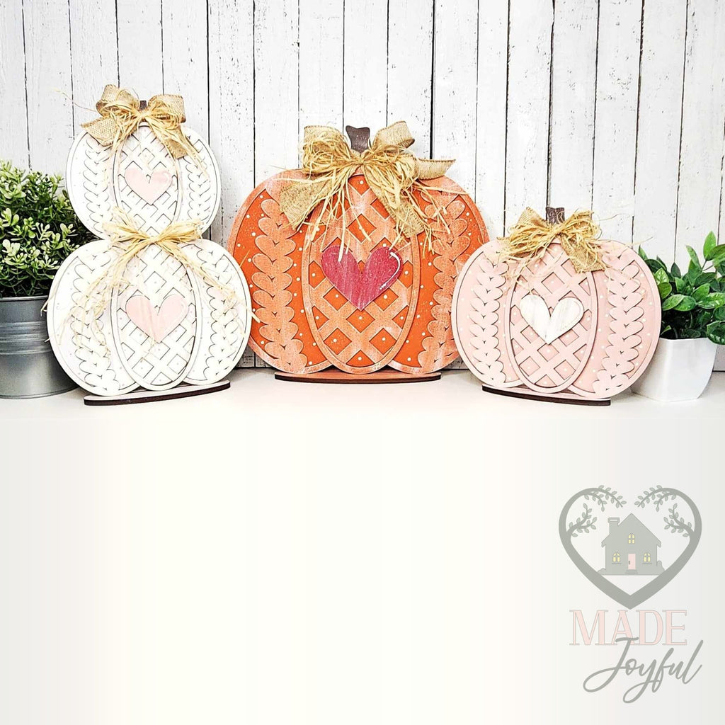 Trio of sweater-knit pumpkin shelf sitters in white, orange, and pink with lattice hearts and burlap bows, hand-painted in Brentwood, TN.