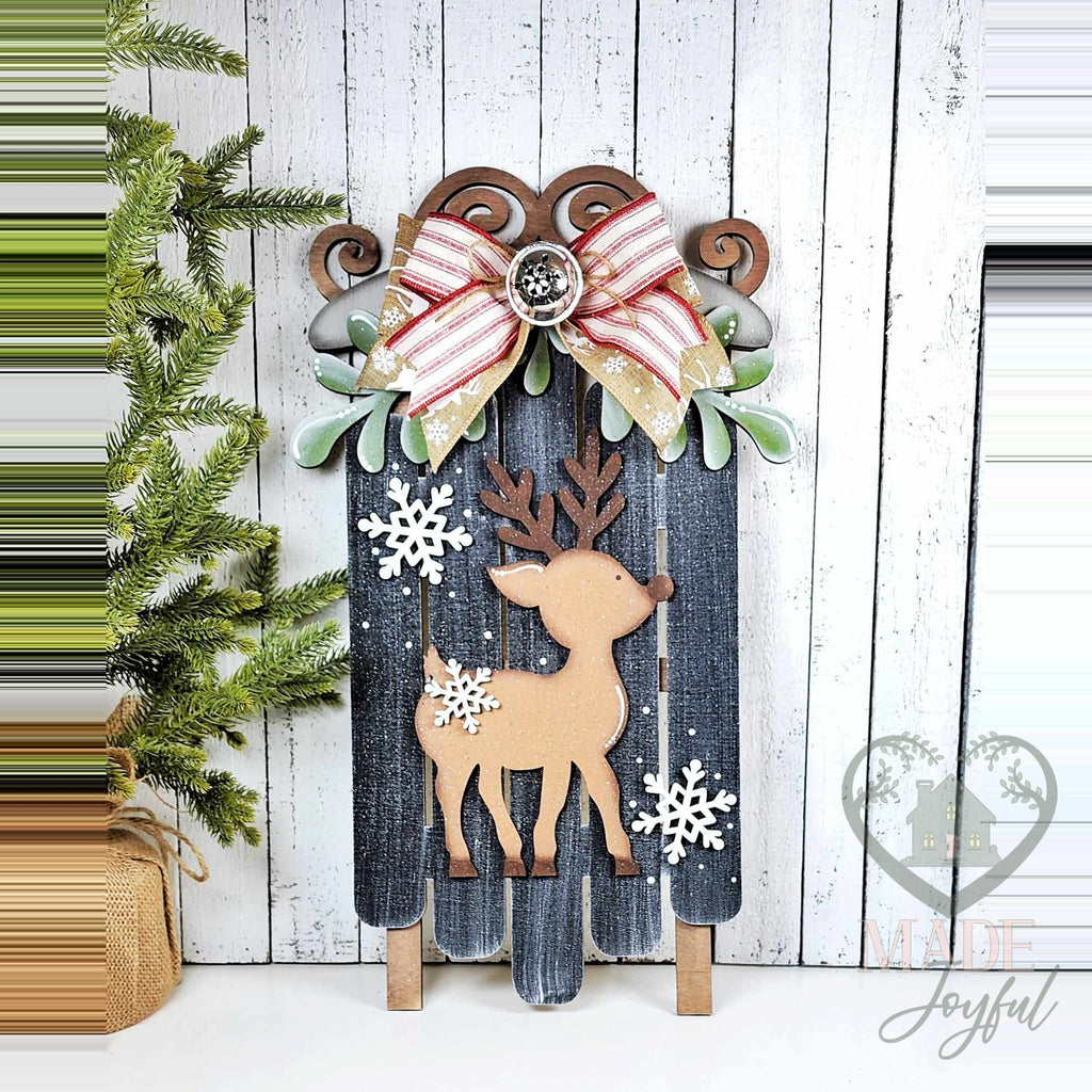 Oh Deer wooden Christmas sled painted navy with a reindeer, snowflakes, and a red striped bow, hand-painted in Brentwood, TN.