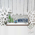 Welcome Winter word art shelf sitter with evergreen trees and a blue cabin, hand-painted in Brentwood, TN.