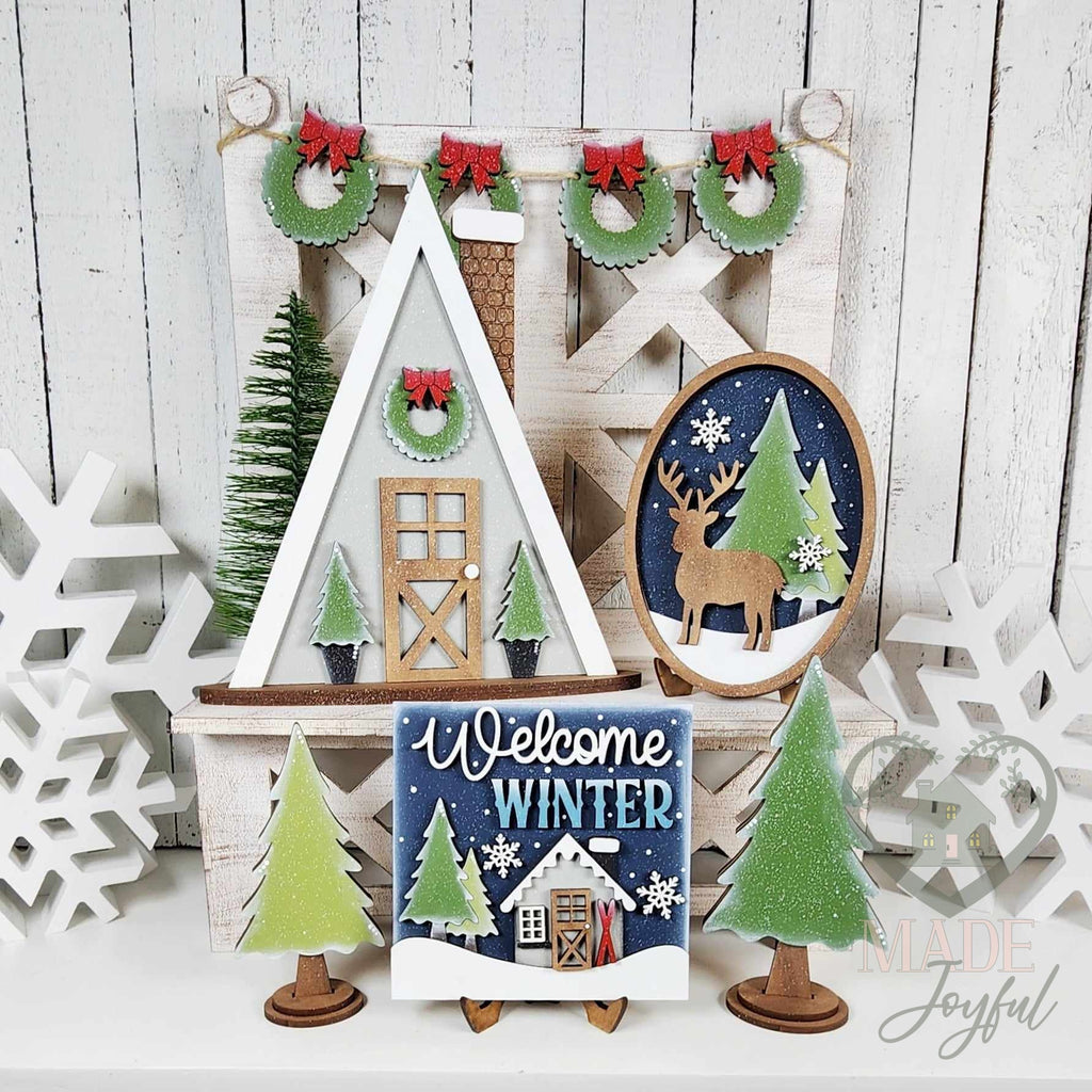 Winter Cabin tiered tray set with A-frame cabin, Welcome Winter sign, deer oval, trees, and wreath banner, hand-painted in Brentwood, TN.