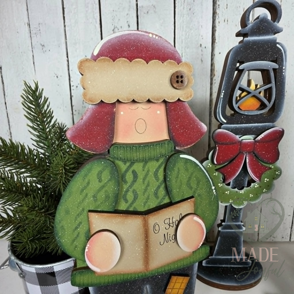 Caroler in green sweater singing from a songbook beside a lamp post, hand-painted in Brentwood, TN.