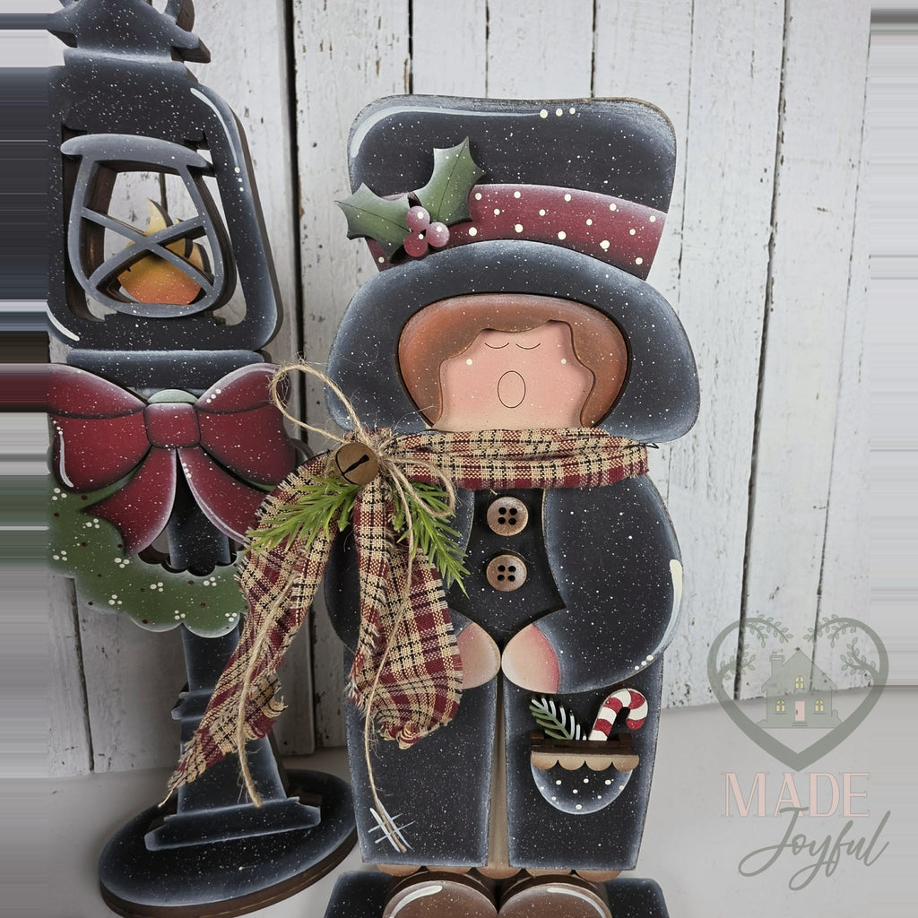 Caroler in black top hat and plaid scarf, hand-painted in Brentwood, TN.