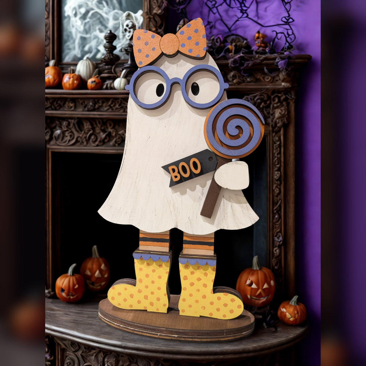 Gertie the Ghost shelf sitter with purple glasses, polka-dot orange bow, swirl lollipop, BOO tag, striped stockings, and yellow polka-dot boots on a Halloween mantel, hand-painted in Brentwood, TN.