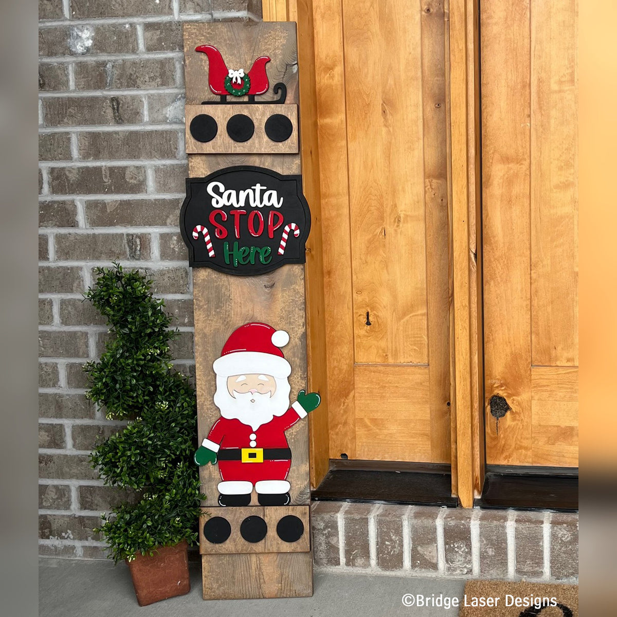 Santa Stop Here interchangeable porch leaner with a sleigh, a Santa Stop Here sign, and a waving Santa on a stained wood base by a front door