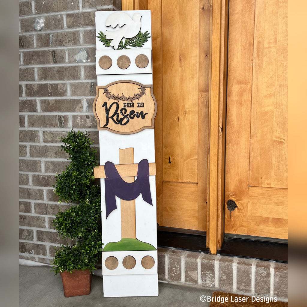 He Is Risen Easter interchangeable porch leaner with a dove, a He Is Risen sign, and a cross draped in purple on a white wood base by a front door