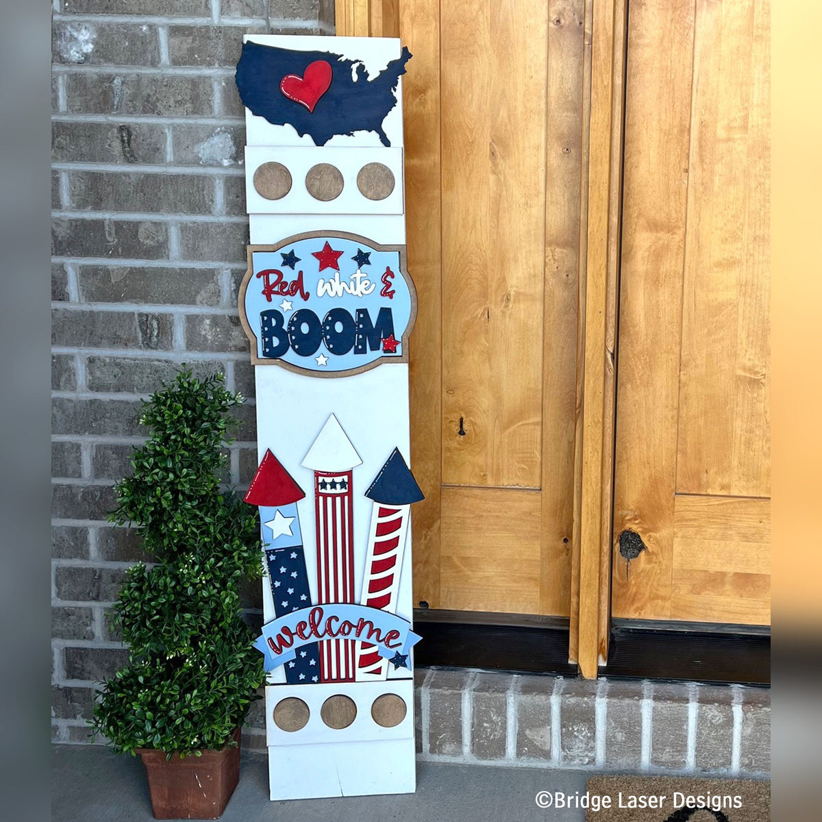 Red White and Boom 4th of July interchangeable porch leaner with a USA map, firework rockets, and a welcome banner on a white wood base