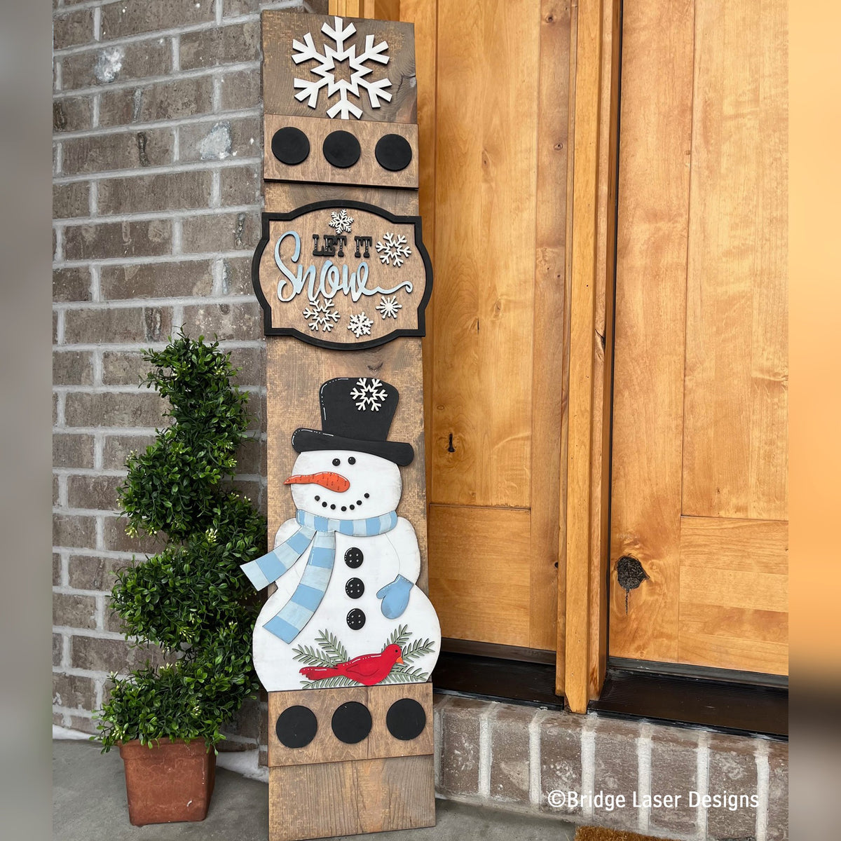 Let It Snow interchangeable porch leaner with a snowflake, a Let It Snow sign, and a snowman in a top hat and scarf on a stained wood base
