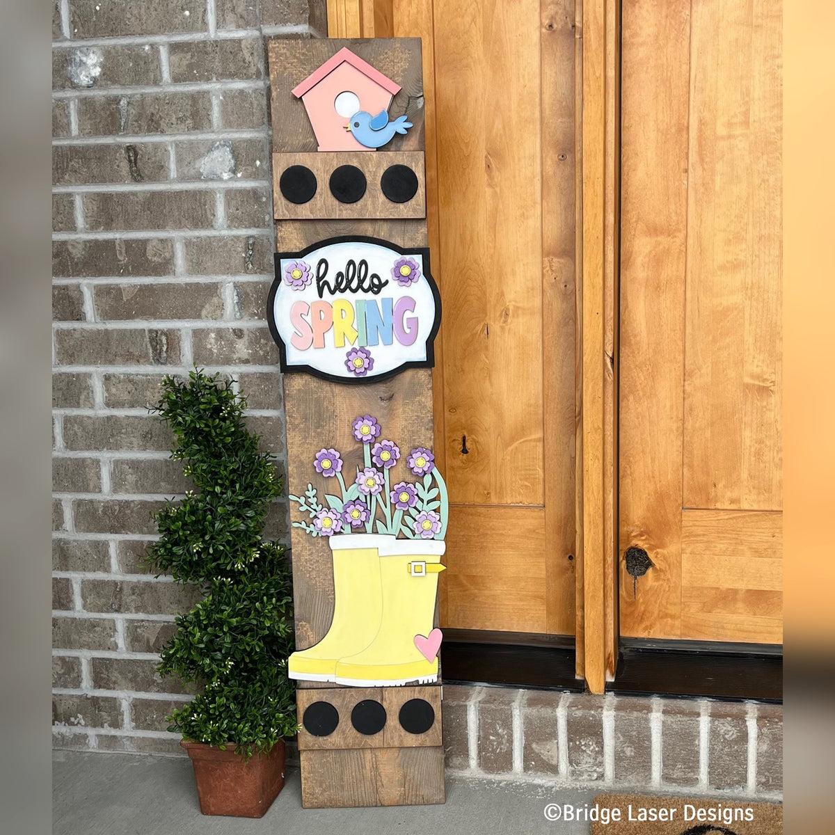Hello Spring interchangeable porch leaner with a birdhouse, a Hello Spring sign, and a yellow rain boot full of flowers on a stained wood base